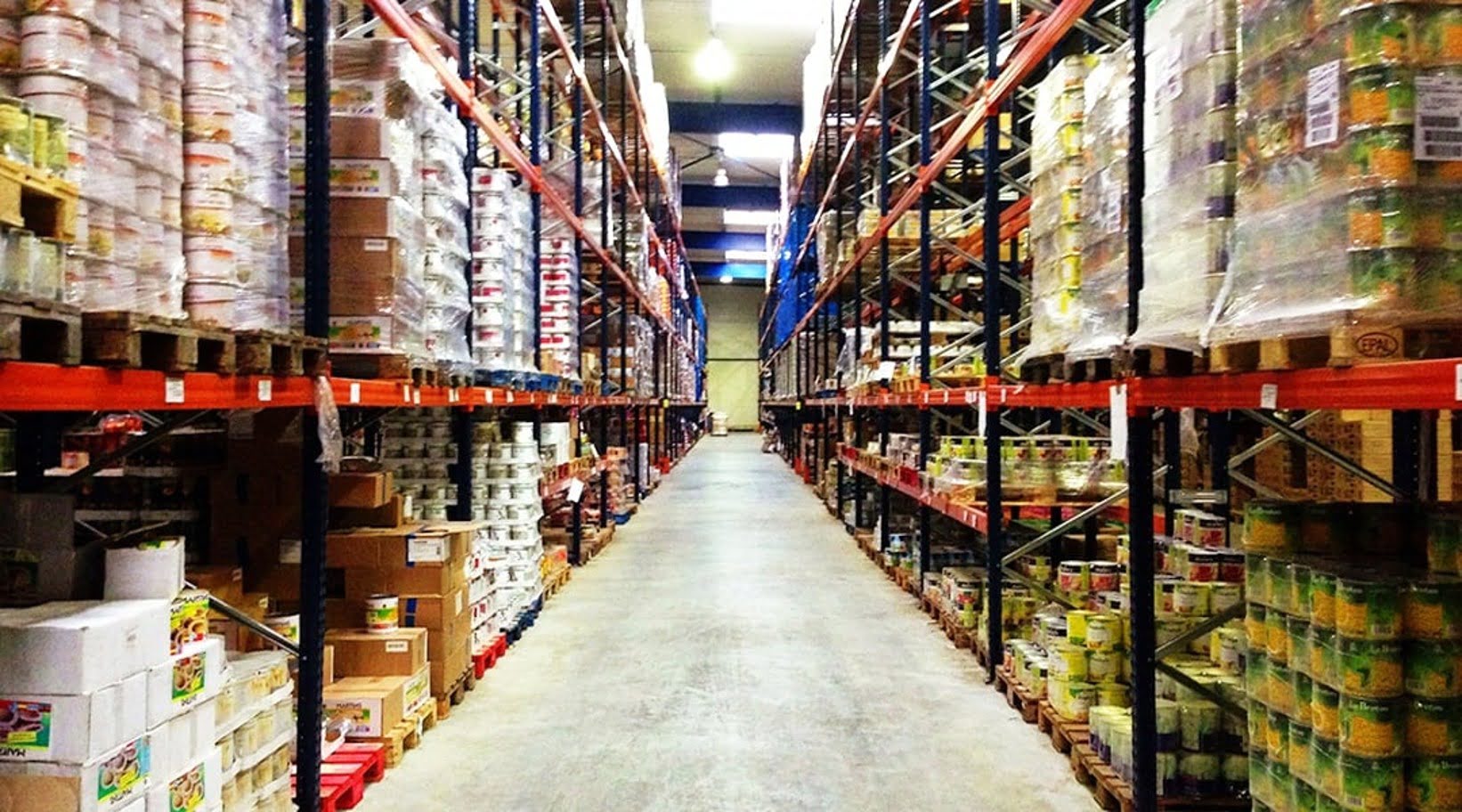 Aisle of a food distribution warehouse stacked with pallets of canned goods