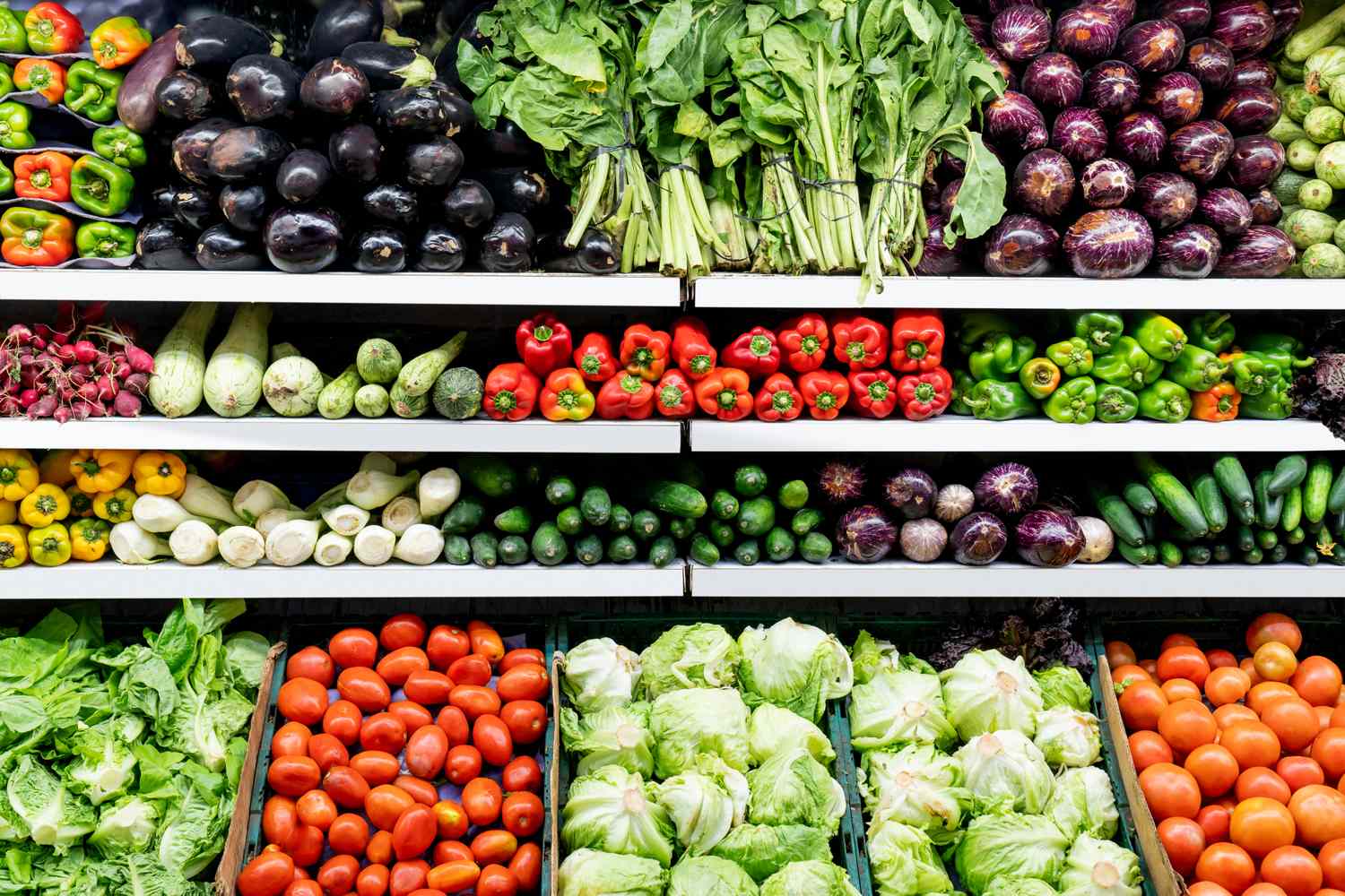 Fresh produce arranged on refrigerated shelves — peppers, aubergines, tomatoes and lettuce