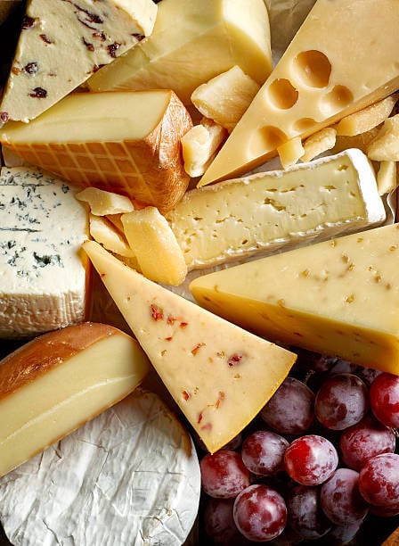 An assortment of speciality cheeses and red grapes on a board